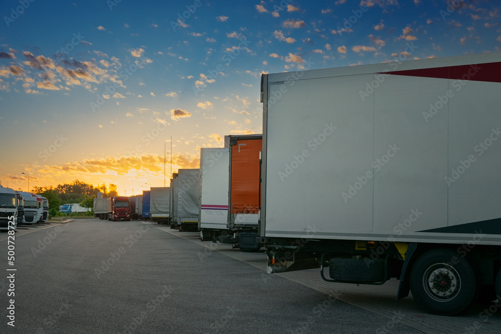 Sun rises over a truck parking lot on the highway. Photo with copy space for your advertisement on the last truck.