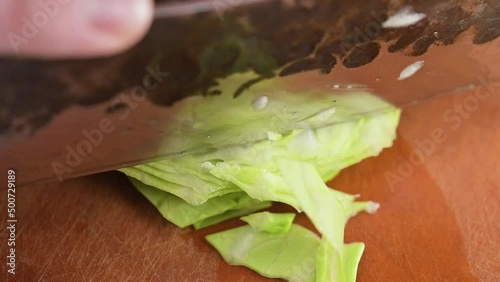 Finely slicing green cabbage up close with a Japanese style chefs knife.  Macro food preparation on cutting board in slow motion.