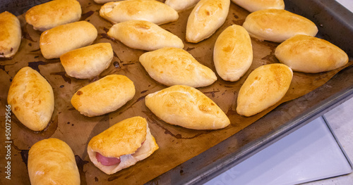 Place the freshly baked pies with the filling on a baking sheet covered with baking paper. Delicious fresh homemade pastries from the oven. Top view