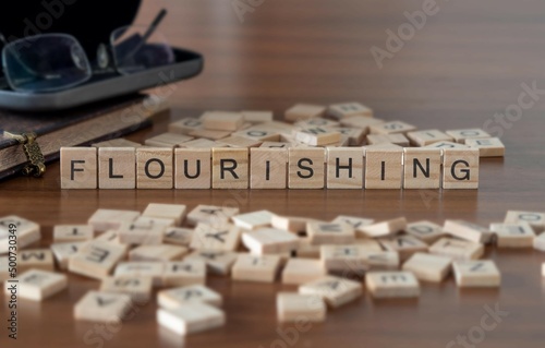flourishing word or concept represented by wooden letter tiles on a wooden table with glasses and a book