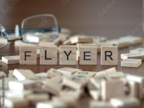 flyer word or concept represented by wooden letter tiles on a wooden table with glasses and a book photo