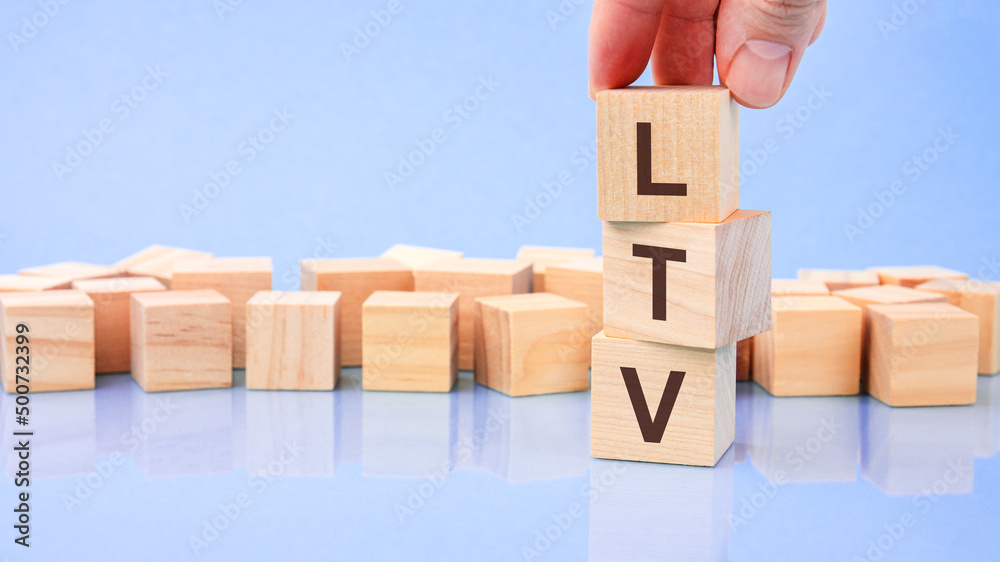 Obraz premium close up image hand of a young businessman holding a wooden cube with letter L. LTV on wooden cube on a blue background with copy space
