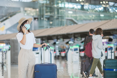 Asian woman tourist woman wearing face mask and using mobile smartphone in airport, protection Coronavirus disease infection. Time to travel after vaccine booster dose concept