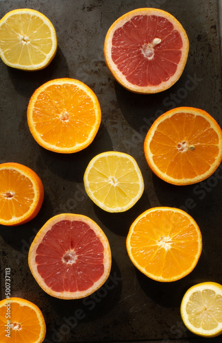 Citrus fruits cut in halves arranged on a dark surface, top view