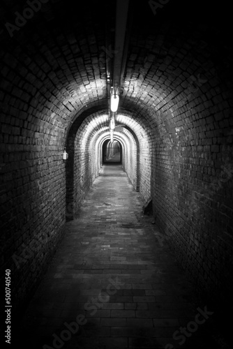 Black and white vertical shot of underground brick tunnel