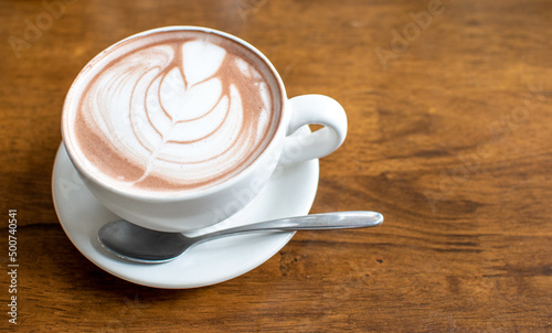 Morning in holiday time to relax with hot coffee and Latte art (Tulip pattern) in a white ceramic cup with stianless steel spoon on old wooden table background in coffee cafe ,Chill out day concept.