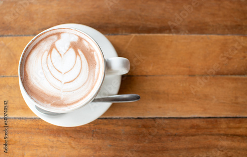 Morning in holiday time to relax with hot coffee and Latte art (Tulip pattern) in a white ceramic cup with stianless steel spoon on old wooden table background in coffee cafe ,Chill out day concept.