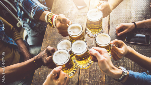 Group of people cheering beer glasses in brewery pub restaurant - Friends celebrating happy hour weekend sitting in bar table - Beverage lifestyle concept