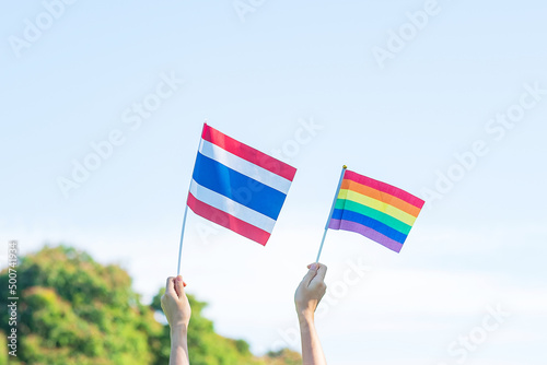 Photography hands showing LGBTQ Rainbow and Thailand flag on nature background