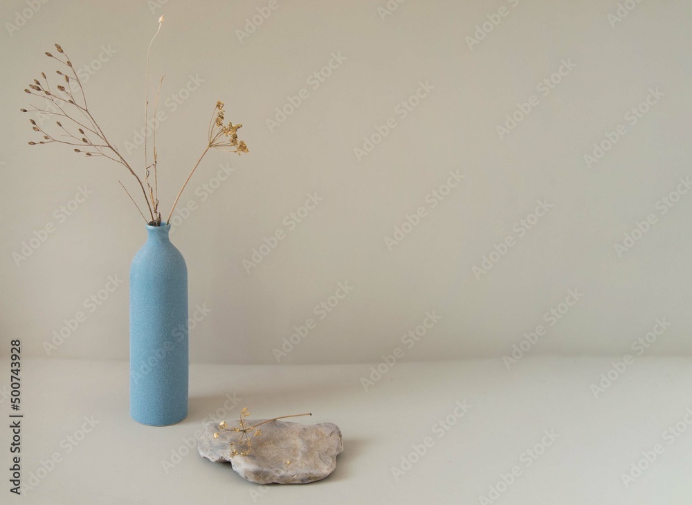 Minimalistic still life with a blue matte vase, dried flowers and a stone on a beige background For product presentation, design, space copy