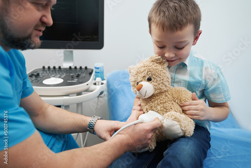 Young boy together with Caucasian doctor examining teddy bear with ultrasound