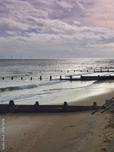 Waves breaking on Frinton Beach, with sunlight breaking through storm clouds overhead to reflect in soft, glowing light from the shimmering sand. photo