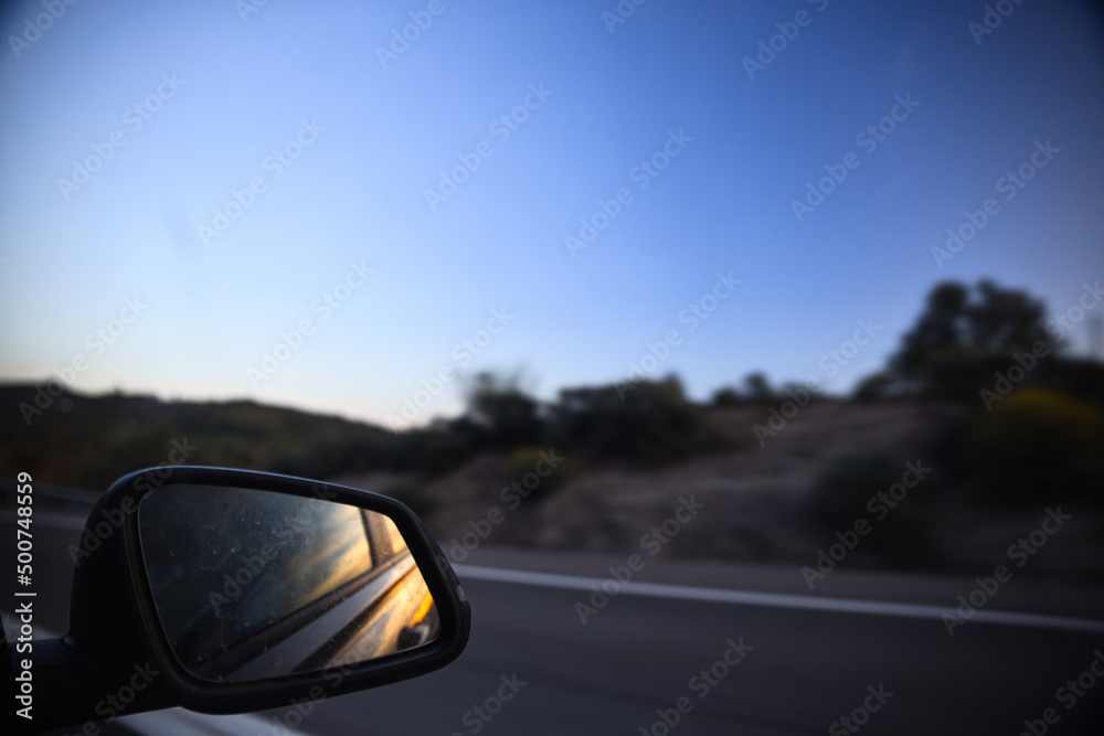 photo of the rear view mirror of a car in motion at sunset
