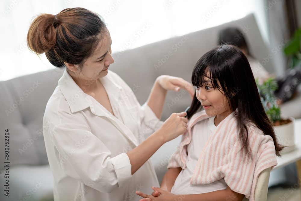 Asian Mother cutting hair to her daughter in living room at home while stay at home safe from Covid-19 Coronavirus during lockdown. Self-quarantine and social distancing concept. Asian Mother cutting hair to her daughter in living room at home while stay at home safe from Covid-19 Coronavirus during lockdown. Self-quarantine and social distancing concept.