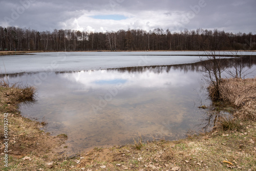 Forest lake coated in the first ice. Autumn landscape of Belarus.