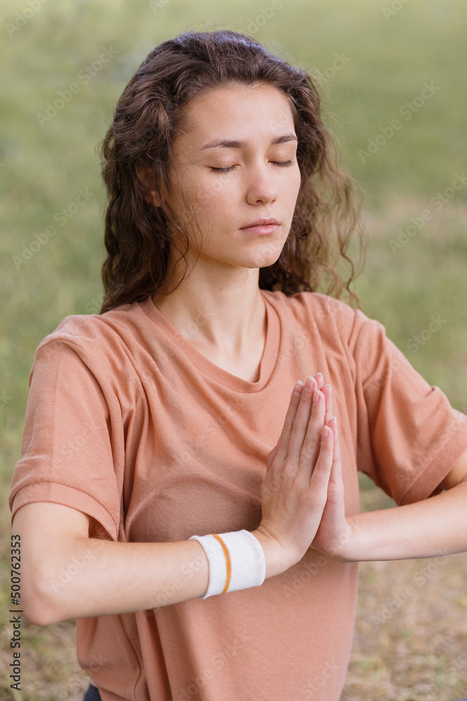 Fototapeta premium a European woman with curly hair meditates in a park. yoga and meditation for mental and physical health. a woman sits in the lotus position and namaste with her eyes closed and engages in breathing
