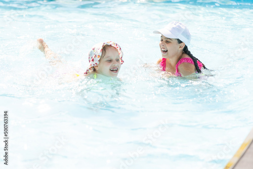 two girls splash in an outdoors swimming pool in summer. Happy children  sister playing  enjoying sunny weather in public pool