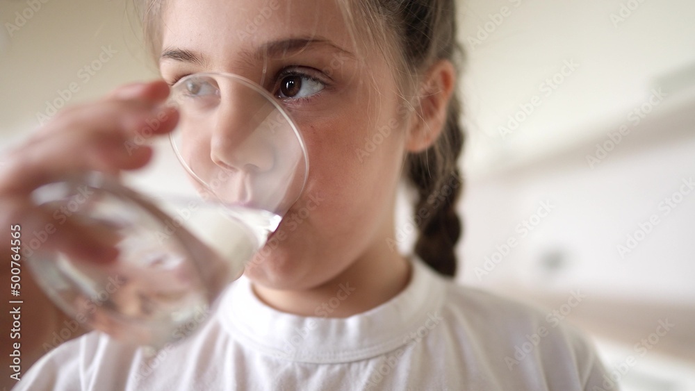 child girl drinking water from a glass cup. the problem of lack of clean drinking water in the world. little girl in the kitchen drinks drinking water from a lifestyle transparent glass cup