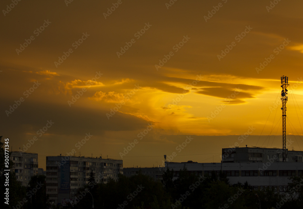 Sunset over a large industrial city with silhouettes of houses and antennas.