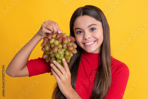 cheerful kid hold fresh grapes fruit on yellow background