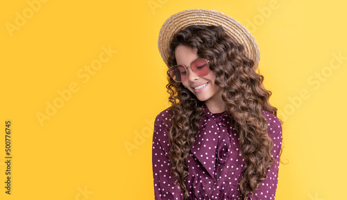 cheerful girl in straw hat and sunglasses with long brunette curly hair on yellow background