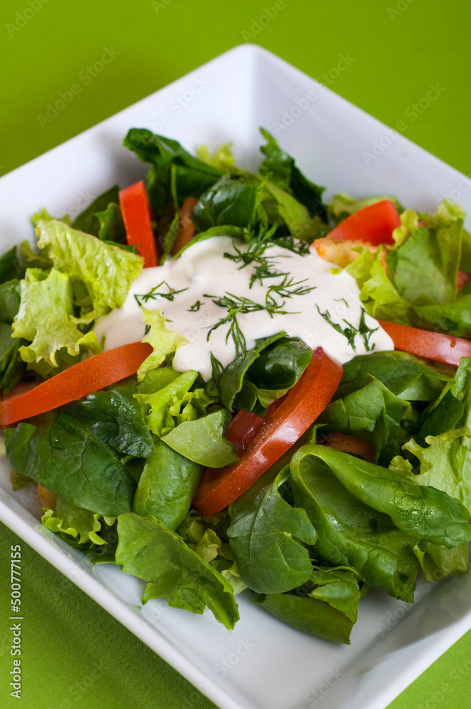 Green vegan summer lettuce with spinach, by tomatoes and sour cream.