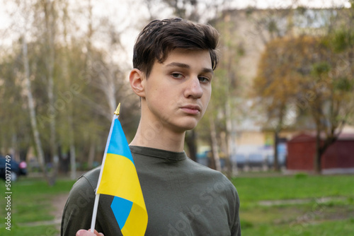 Young boy holding Ukrainian flag on spring nature background, lonely patriot man standing, looking towards you with blue, yellow fabric flag of Ukraine. Patriotc teenager Yellow-blue symbol