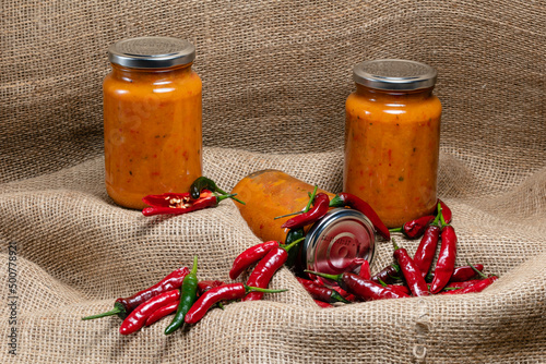 Three bottles of homemade chilli sauce with fresh red jalapinos on a canvas background photo