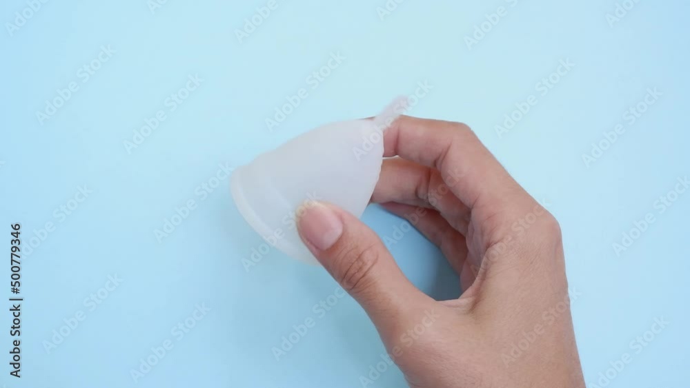 A woman holds a menstrual cup in her hands. White menstrual cup on a blue background. close-up of a hand showing a menstrual cup. Zero waste concept. An alternative feminine hygiene product in the per A woman holds a menstrual cup in her hands. White menstrual cup on a blue background. close-up of a hand showing a menstrual cup. Zero waste concept. An alternative feminine hygiene product in the per