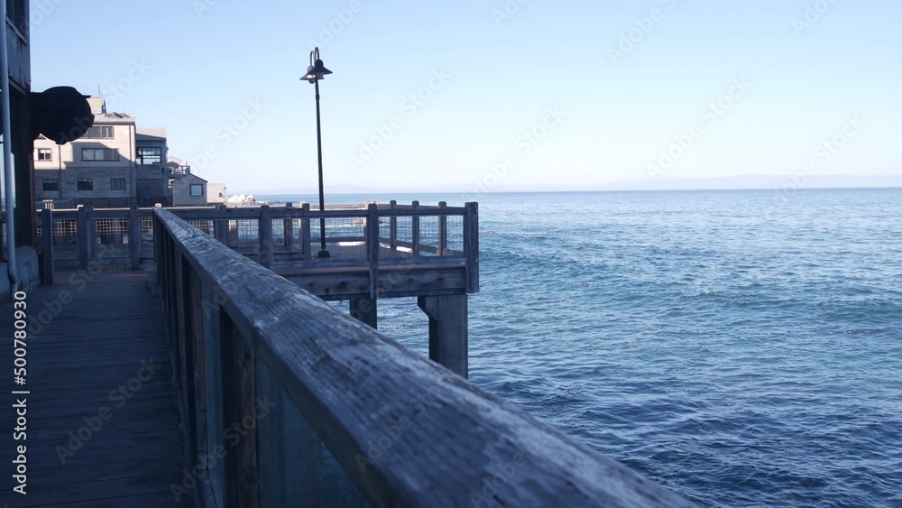 Waterfront wooden boardwalk in Monterey, California USA. Beachfront promenade on piles, pillars or pylons by ocean sea water and bay aquarium on Cannery Row street. Tourist vacations waterside resort.