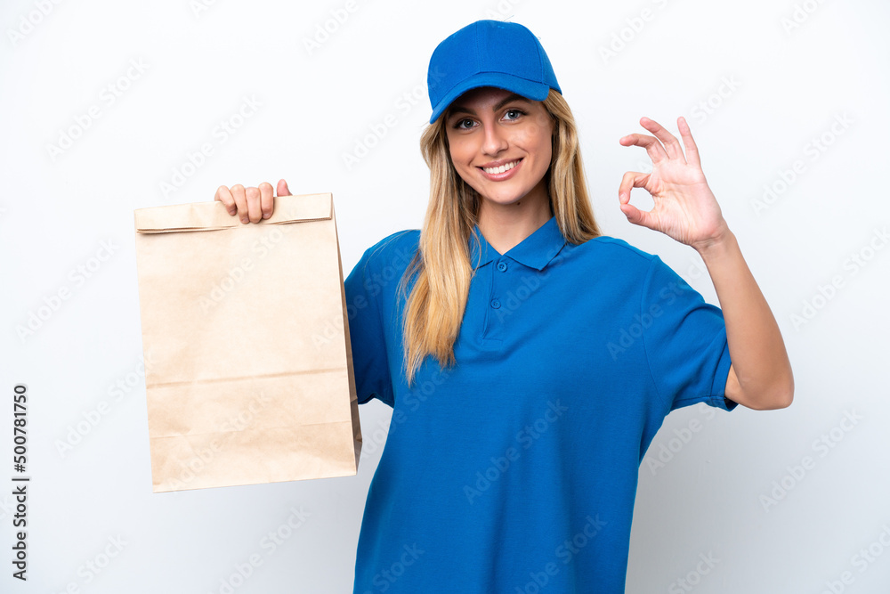 Young Uruguayan woman taking a bag of takeaway food isolated on white background showing ok sign with fingers Young Uruguayan woman taking a bag of takeaway food isolated on white background showing ok sign with fingers