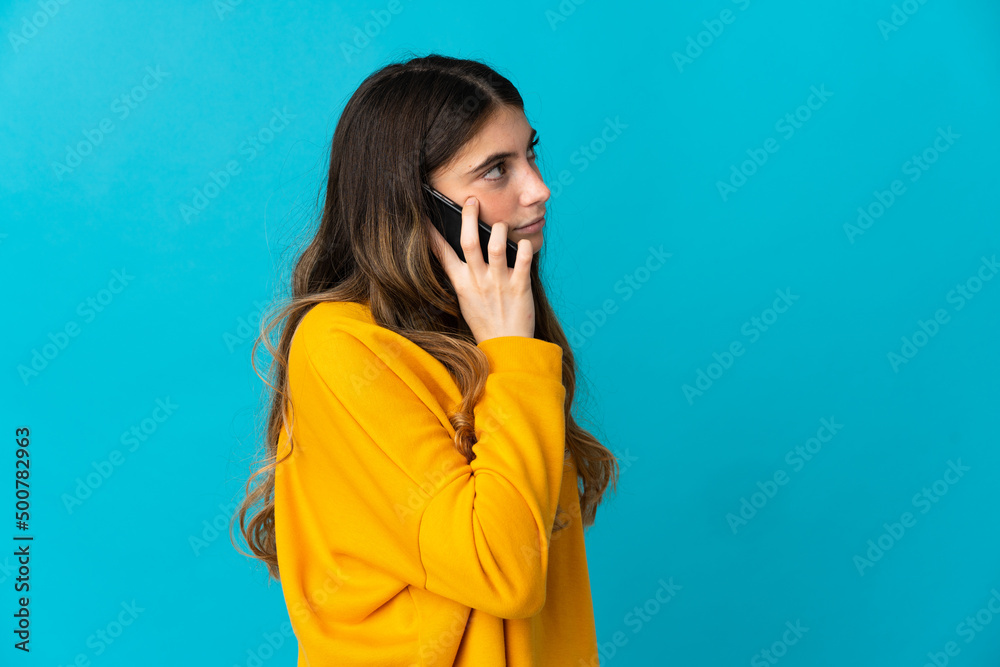 Young caucasian woman isolated on blue background keeping a conversation with the mobile phone with someone