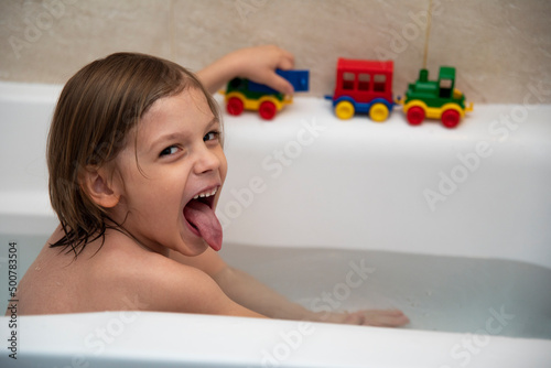 Sześcioletni chłopiec bawiący się w kąpieli plastikowymi samochodami photo