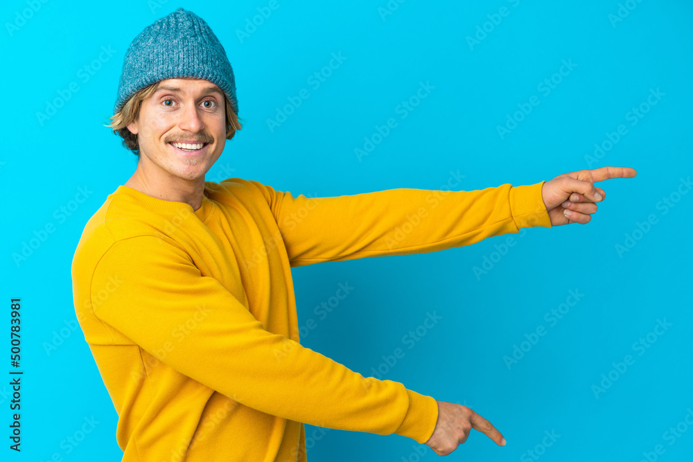 Handsome blonde man isolated on blue background pointing finger to the side and presenting a product