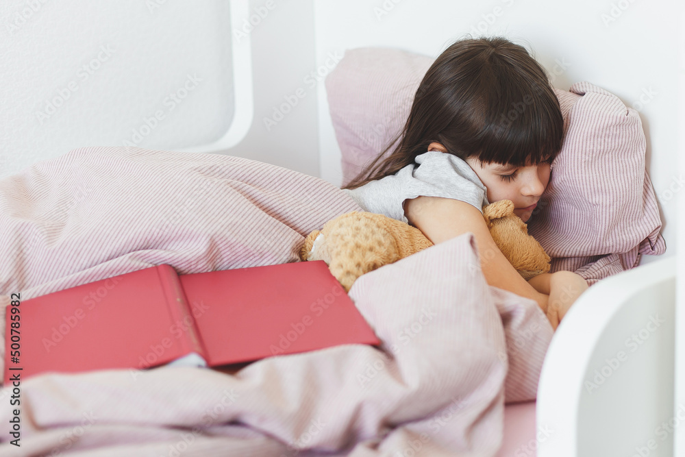 toddler girl read and looked at a book and fell asleep in her bed, childhood concept. toddler girl read and looked at a book and fell asleep in her bed, childhood concept.