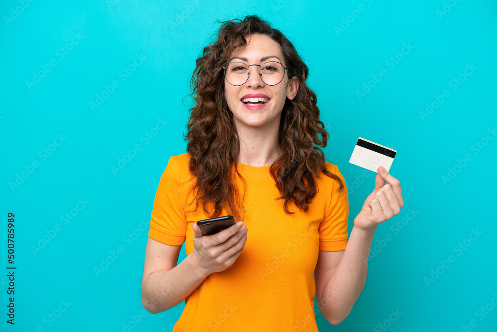 Young caucasian woman isolated on blue background buying with the mobile with a credit card Young caucasian woman isolated on blue background buying with the mobile with a credit card