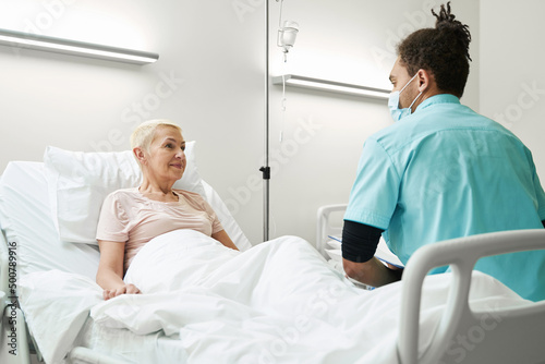 Doctor listening to old woman in hospital bed
