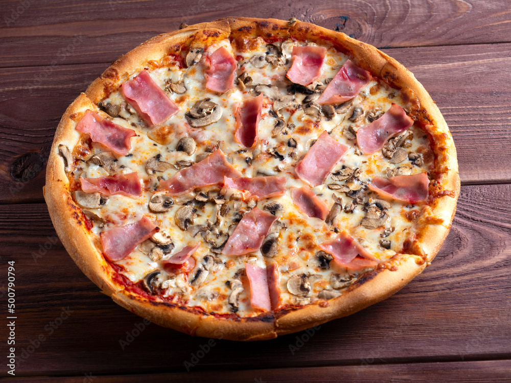Close-up pizza with ham and mushrooms on a brown wooden background. A traditional Italian dish. Top view, flat lay