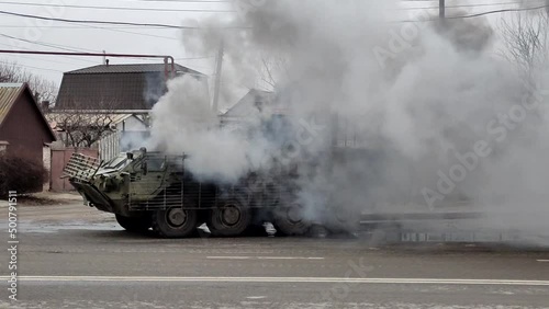 Burning armored personnel carrier with grey smoke cloud on Ukrainian city street. War in Ukraine