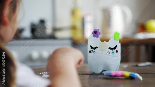 Caucasian preschool girl doing crafts with plastic bottle and paints. Recycle upcycling waste. Sustainable lifestyle