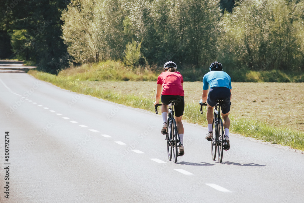 Two professional cyclist racers, male and female during training on a paved road through the mountain landscape, front view.