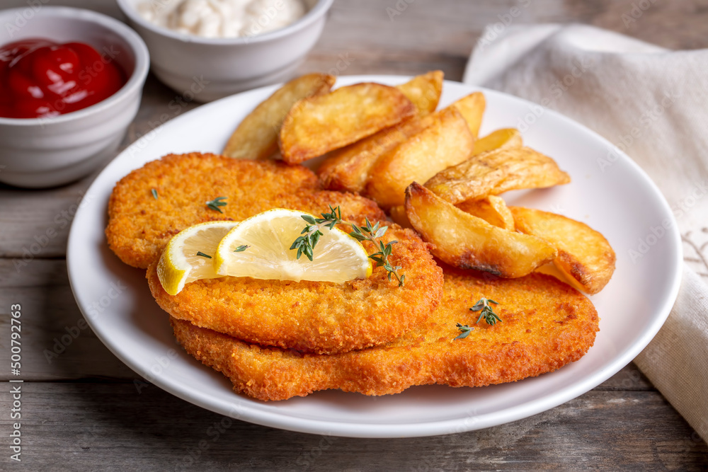 Chicken schnitzel with sauce, fried potatoes and lemon in a plate Chicken schnitzel with sauce, fried potatoes and lemon in a plate