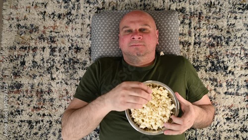 Man is getting bored waiting for a movie to start so he is starting to play a silly game with a bowl of popcorn. He is throwing up popcorn and trying to catch it with his mouth until losing his cool