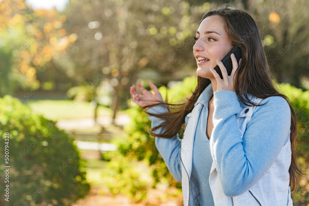 Beautiful teenage girl talking on her mobile phone in a park