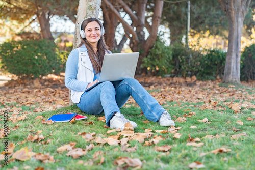 beautiful teenage student using her computer sitting next to a tree in the park