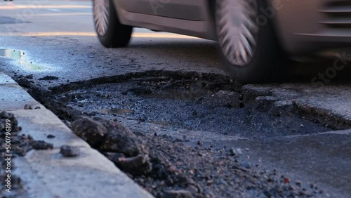 Vehicles Driving Over Large Erosion Damage Hole in City Street Asphalt after Severe Weather and Heavy Rainfall Creating Risk of Damaging Car Tyre and Suspension