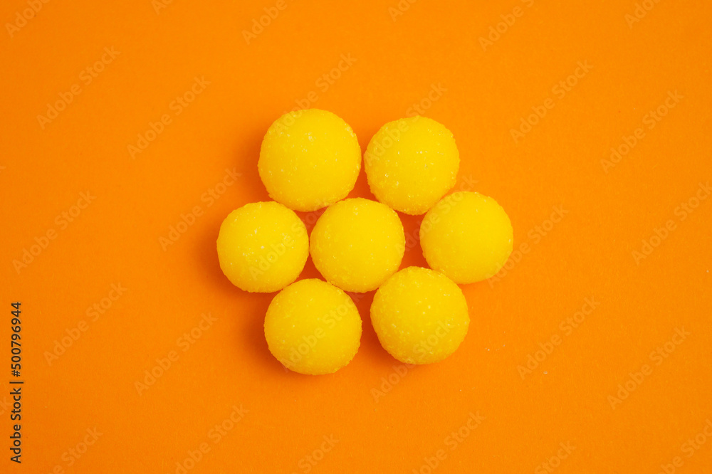 Yellow candy drops in sugar on an orange background. Laid out in the shape of a flower. Place for the inscription. Yellow candy drops in sugar on an orange background. Laid out in the shape of a flower. Place for the inscription.