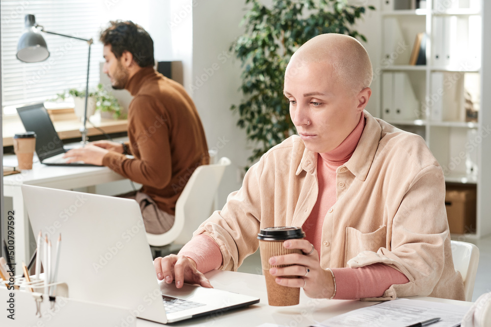 Content young Caucasian businesswoman in casual outfit drinking coffee and using laptop while working online Content young Caucasian businesswoman in casual outfit drinking coffee and using laptop while working online