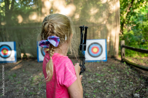 Young girl at summer camp learning to use a bow and arrow looking down field at the target. photo