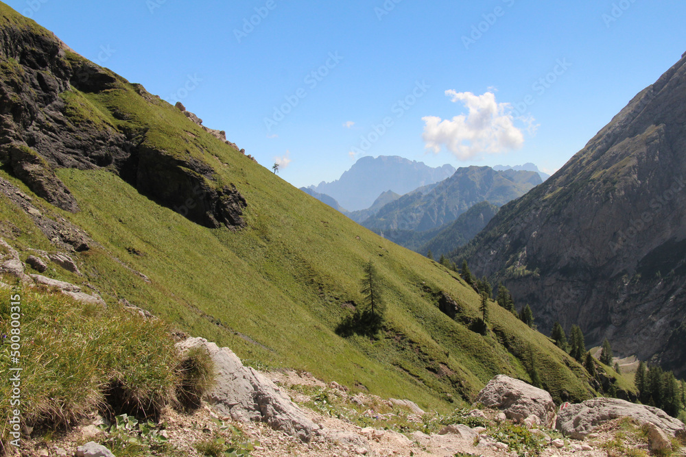 Mountain landscape with green slope and mountain massif on background in a sunny day. Italian Alps.